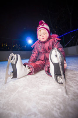 girl in skates sit on ice rink after fall