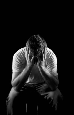 young desperate man suffering with hands covering face in deep depression, pain , emotional disorder, grief and desperation concept isolated on black background with grunge studio lighting in black and white
