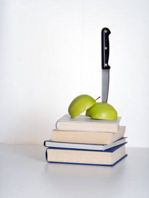 stack of books and apple stabbed by knife to represent education cuts