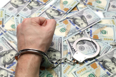 Hand in handcuffs on a pile of dollars