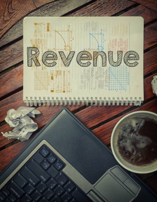 Notebook with text inside Revenue on table with coffee, laptop p